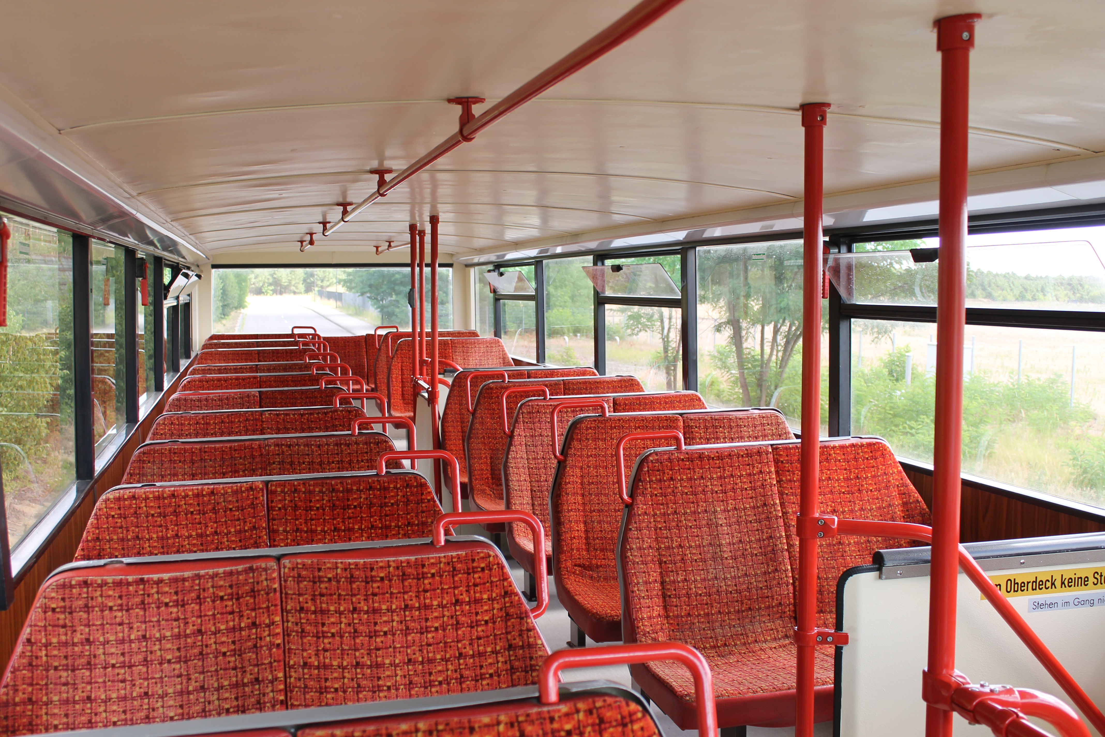 Oberdeck des Doppeldeckerbusses mit Sitzreihen in rot gemustertem Stoff und Panoramafenstern