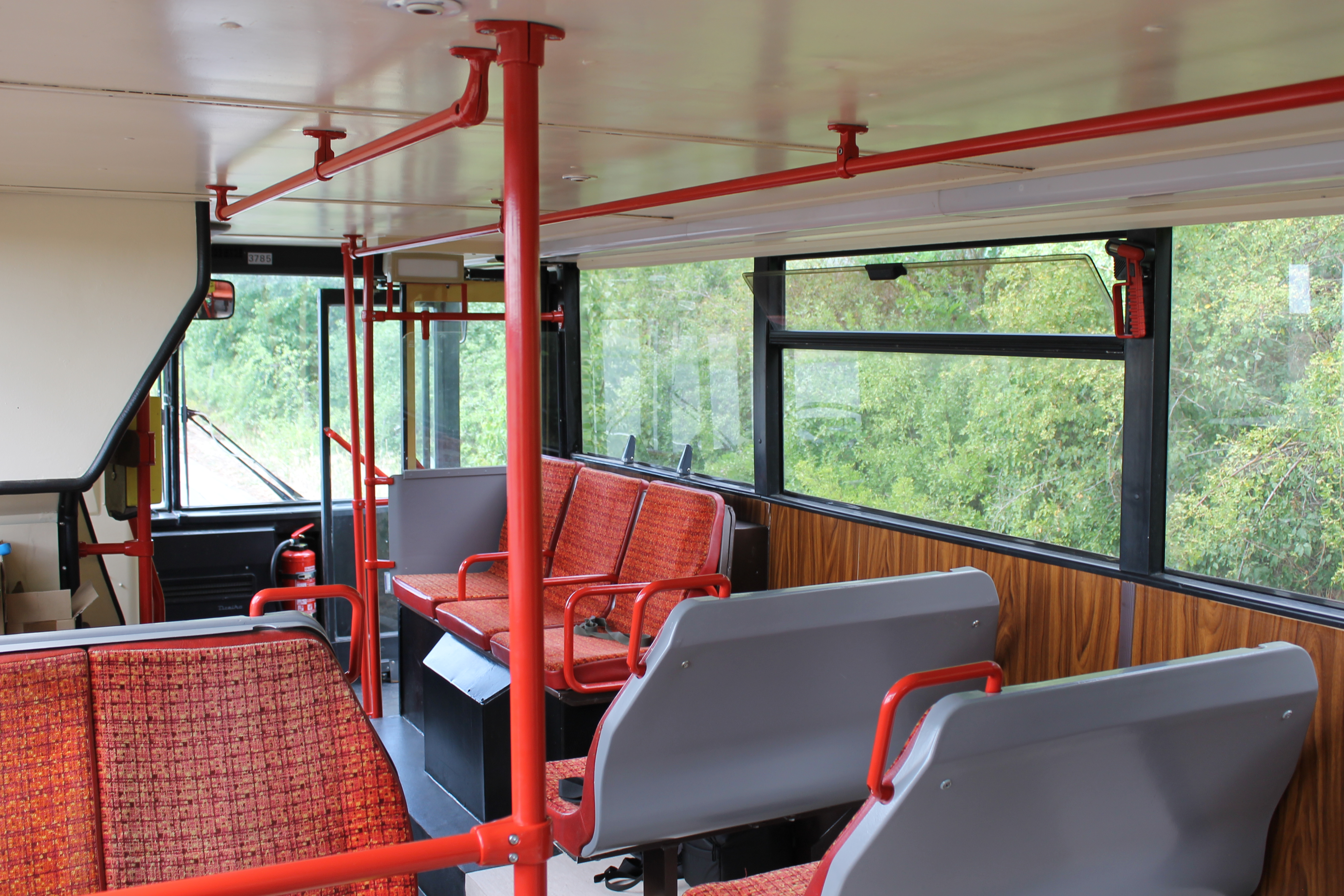 Einstiegsbereich im Bus mit Sitzen, roten Haltestangen und Holzverkleidung